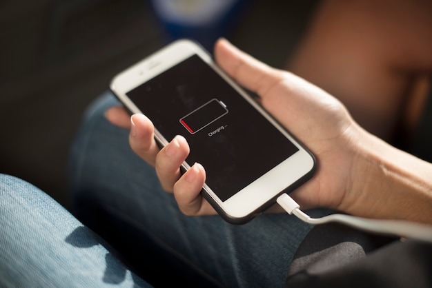 Mains tenant un smartphone branché en charge sur une table